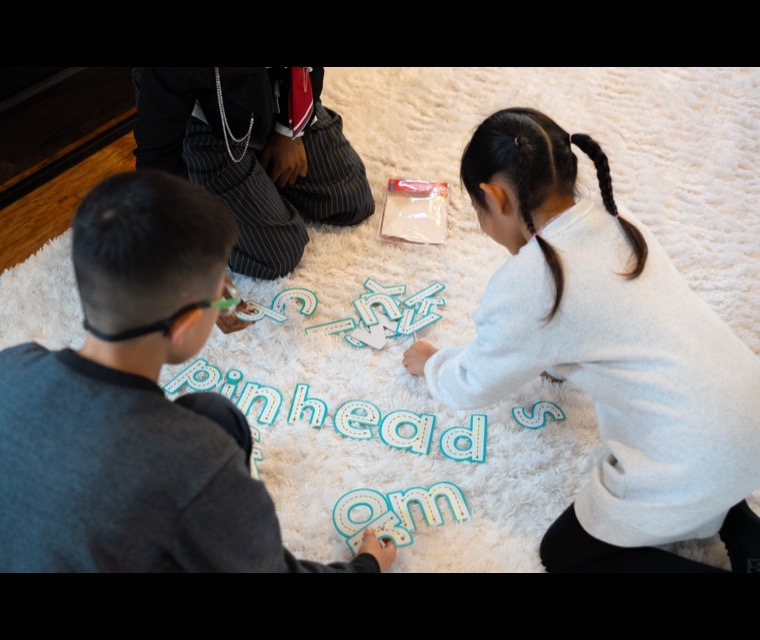 Two children forming letter shapes together on the floor
