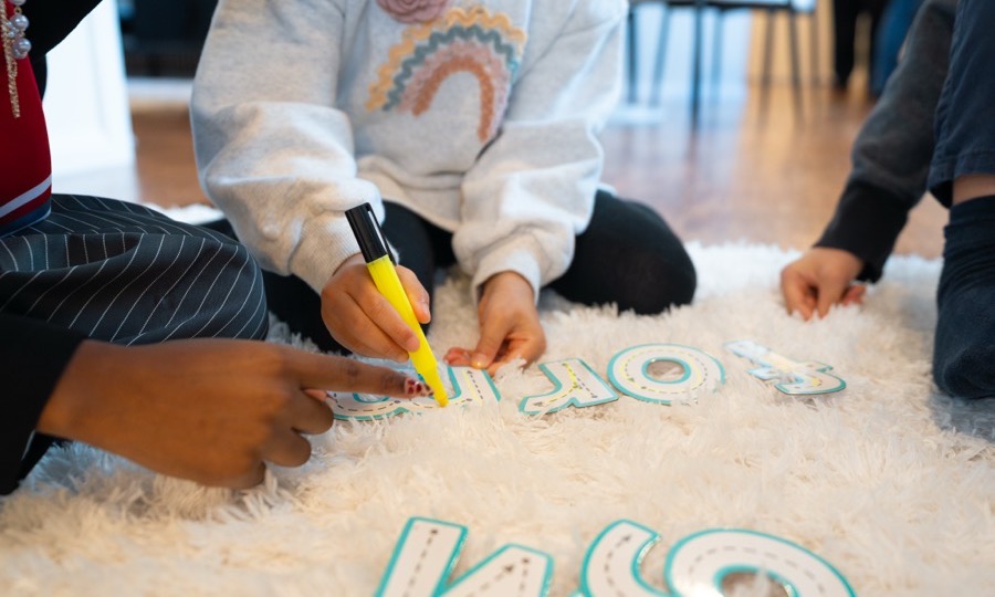 A child exploring textured letter shapes with their hands on a soft rug