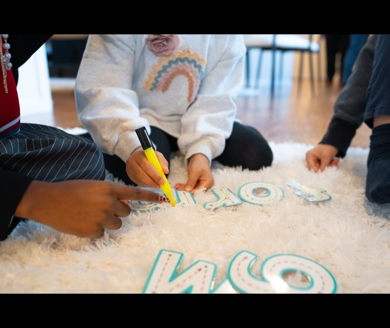 A child exploring textured letter shapes with their hands on a soft rug